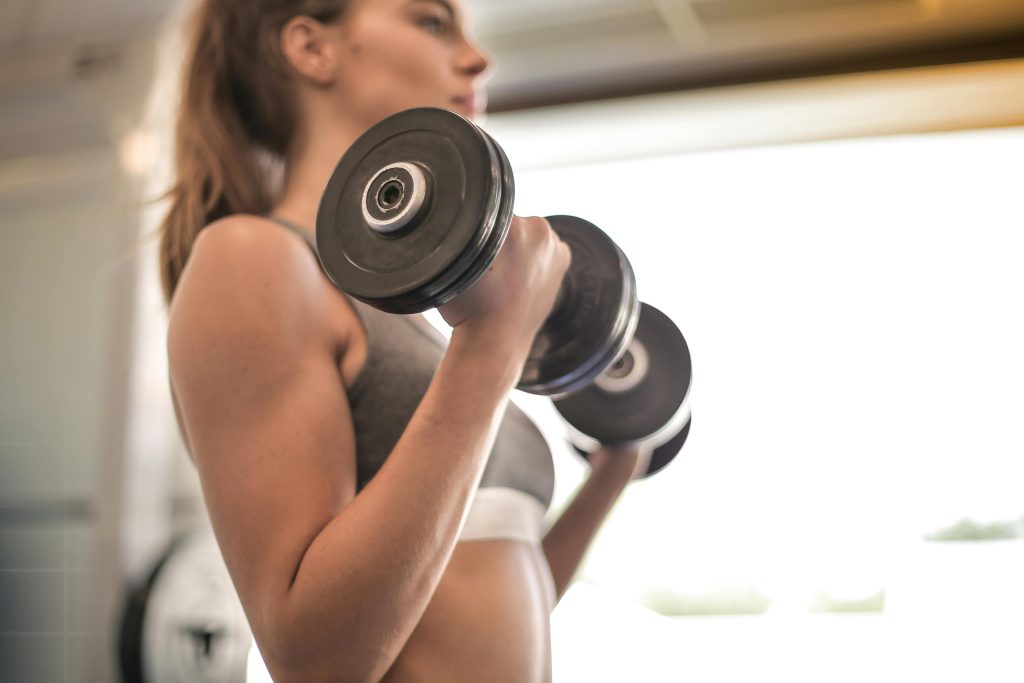 pexels-photo-3757376-3757376 Focused woman lifting dumbbells in a bright gym, emphasizing strength and fitness.
